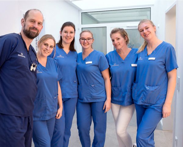 Team des Zahnzentrums Deichkrone steht gemeinsam lächelnd in der Praxis